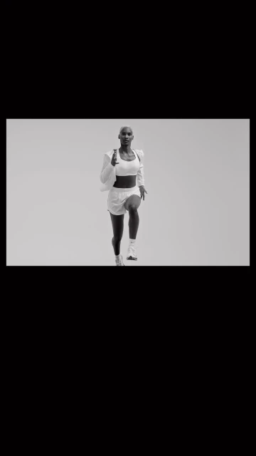 Athletic woman in white workout clothes running indoors against a neutral background in a fitness or sports context.