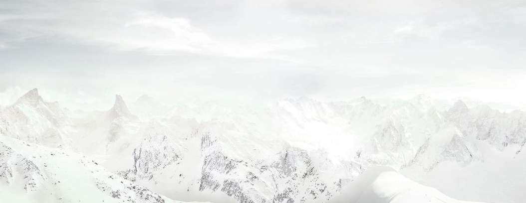 Panoramic vista of snow-covered mountain range under an overcast sky, showcasing a vast and serene winter landscape.