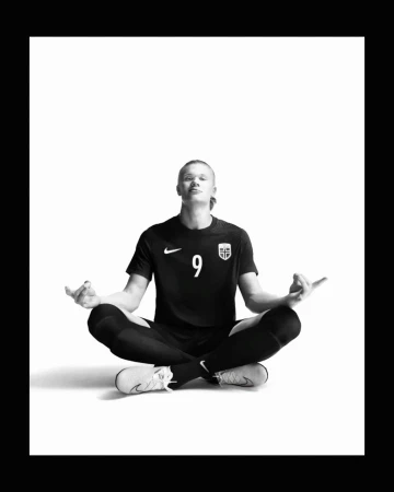 Monochrome image of a blonde soccer player in athletic wear sitting cross-legged with a serene expression, symbolizing focus and balance.