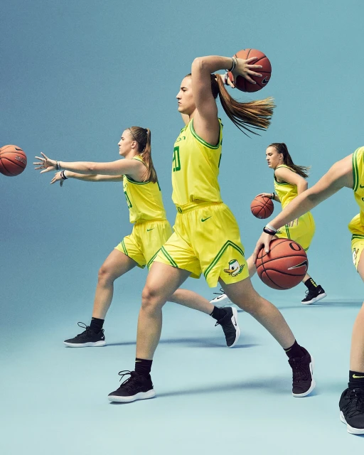 Multiple female basketball players in yellow uniforms dribble and pass basketballs on a light blue studio background, motion blur.