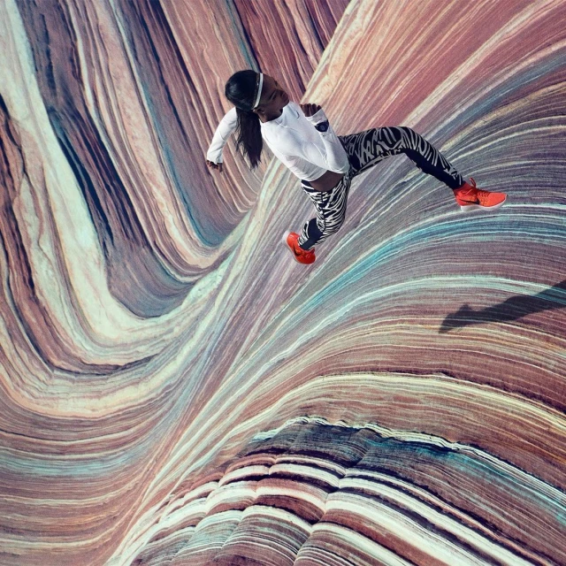A slender woman jumps in front of a wave-like background, wearing a white top, patterned leggings, and orange sneakers in a dynamic pose.