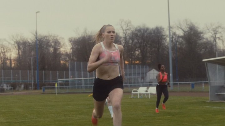 Two adult females running outdoors in sportswear, one light-skinned with blond hair and one dark-skinned with a ponytail, during the day.