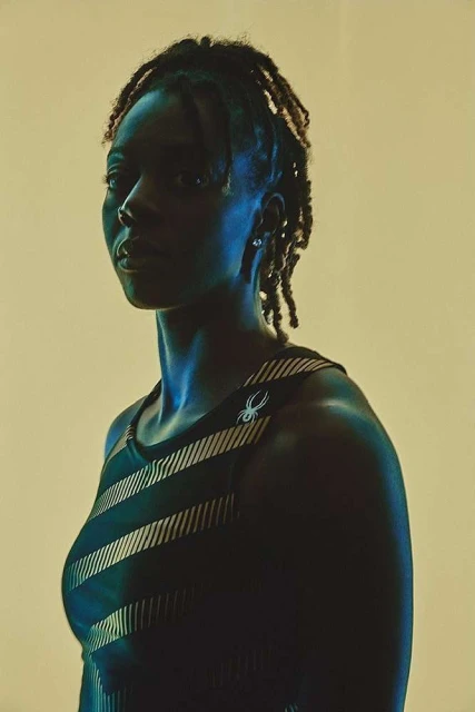Portrait of athletic, young, Black woman in a striped workout top against a neutral background with strong side lighting. 