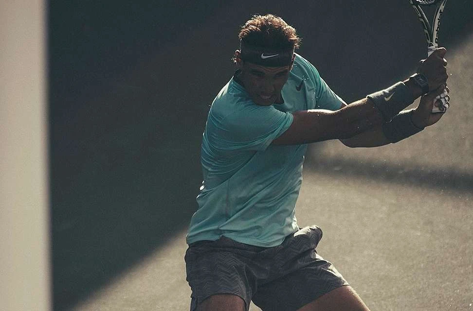 Professional tennis player in action, Rafael Nadal, swinging his racket during a match with a determined facial expression.