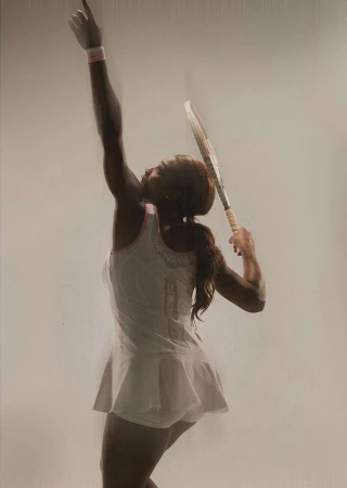 An adult female tennis player in a white tennis dress is in mid-swing with a tennis racket held high on a light background in a studio shot.