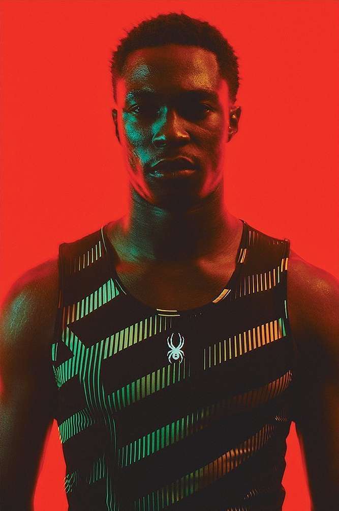 Portrait of an adult male in a black and patterned sports top against a vibrant red backdrop, showcasing fitness and athletic wear.