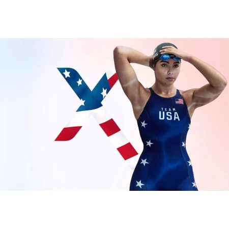 Female athlete in blue USA swimsuit and swim cap adjusting goggles, with an American flag graphic overlay on a white background.