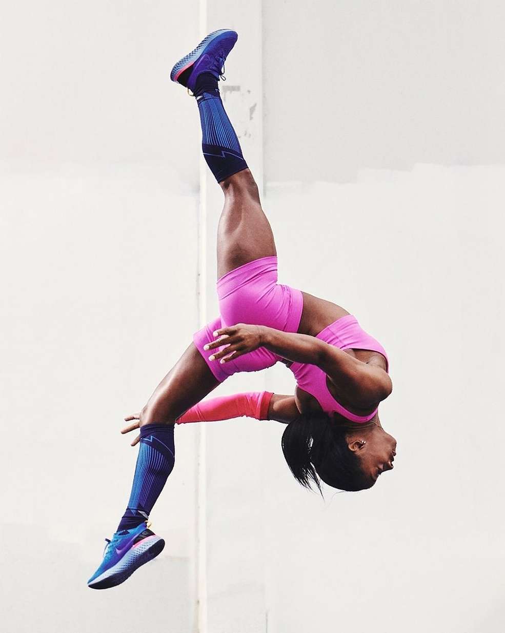 Female athlete performs a backflip against a plain background, showcasing physical fitness in sportswear, training, and body control.