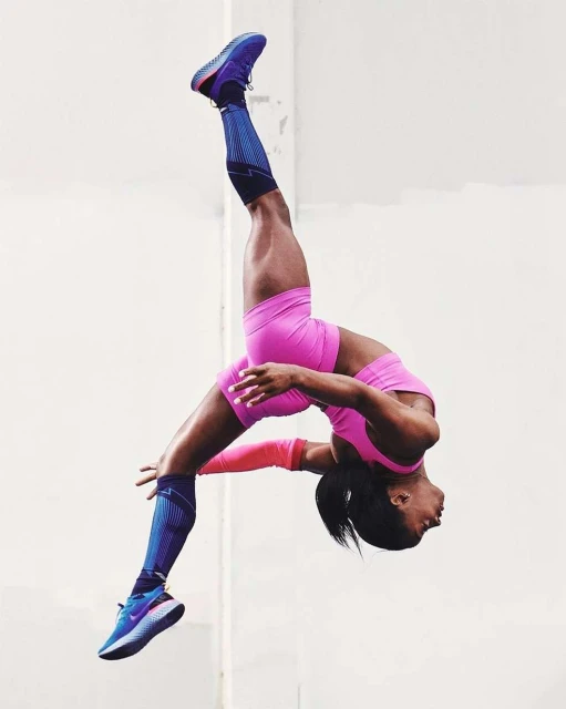 Female athlete performs a backflip against a plain background, showcasing physical fitness in sportswear, training, and body control.