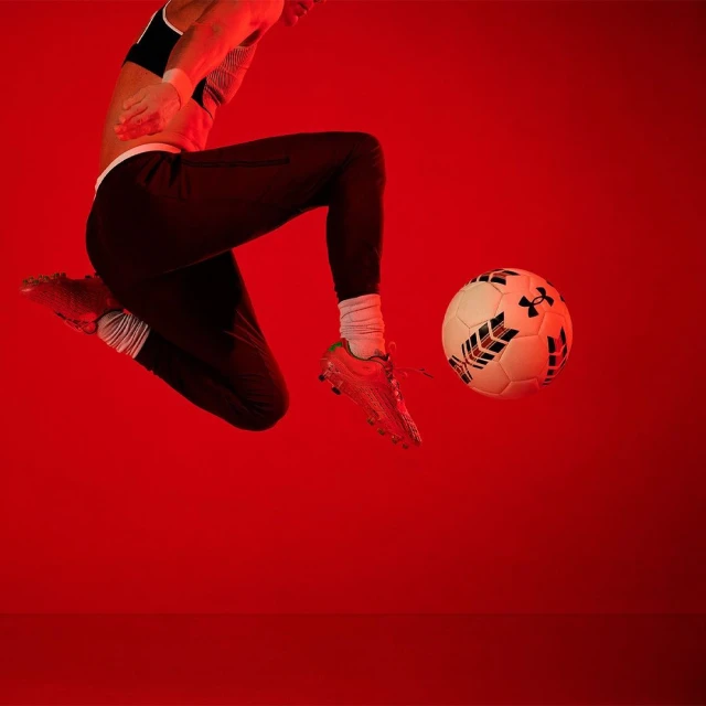 A person in athletic wear leaps with a soccer ball in front of a red background, showcasing a dynamic sports moment with focused lighting.