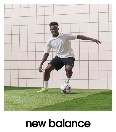 Athletic Black male soccer player in sportswear showcasing a soccer ball on a green field against a gridded white background inside.