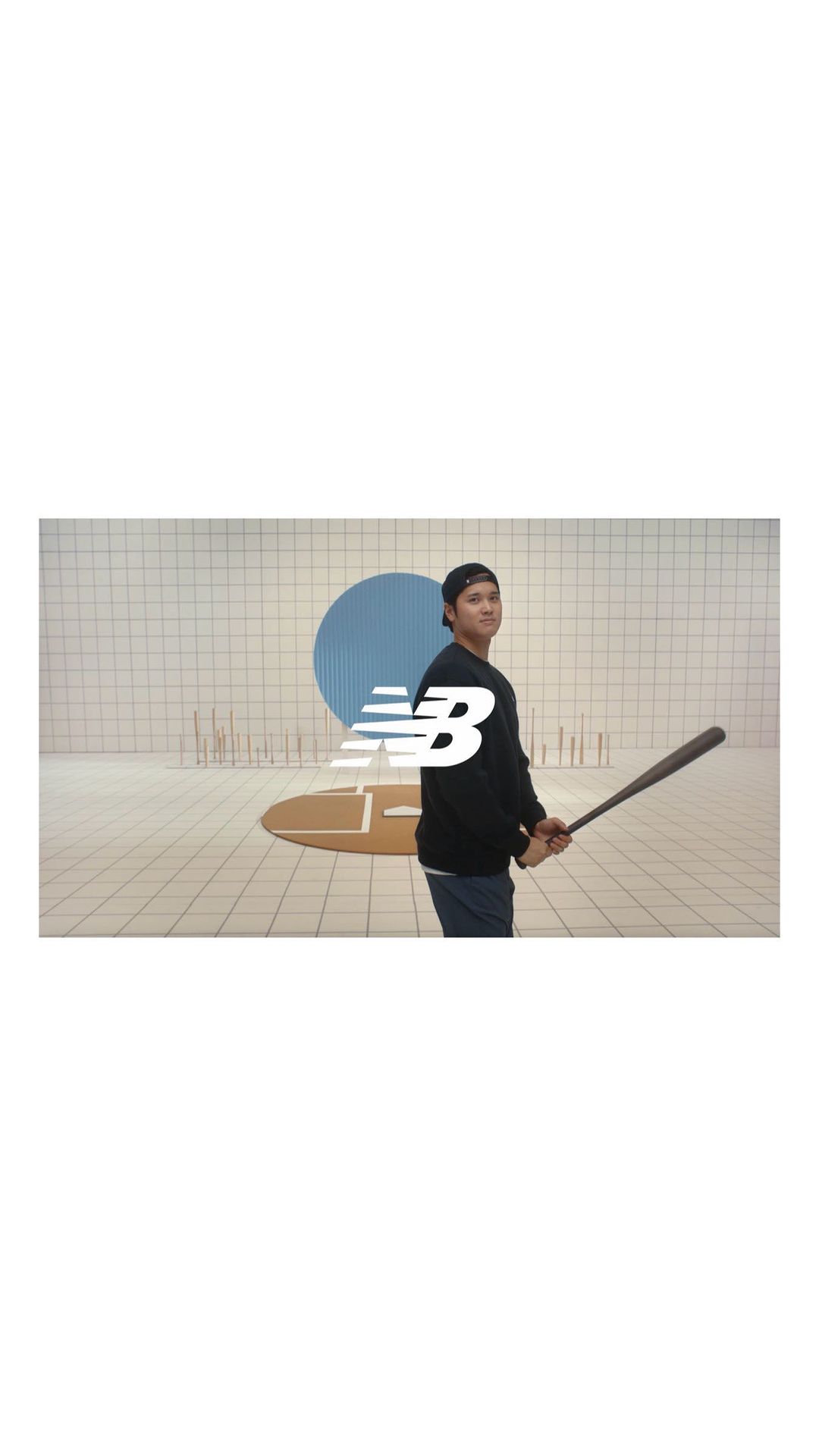 Man with a baseball bat in a casual outfit. New Balance logo in the foreground, set against a white-tiled wall with a blue circle accent.
