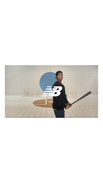 Man with a baseball bat in a casual outfit. New Balance logo in the foreground, set against a white-tiled wall with a blue circle accent.