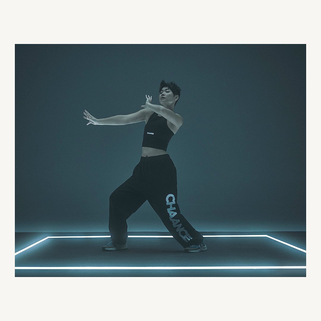 Male dancer in dark athleisure wear poses expressively against a dark backdrop with glowing lines. Modern dance and fashion concept.