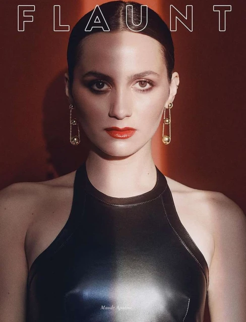 Portrait of Maude Apatow on a magazine cover with red background. She wears a black halter top and long safety pin earrings.
