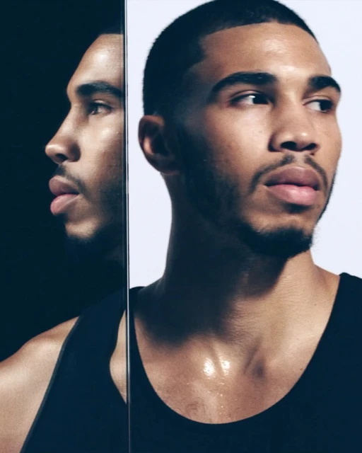 Portrait of a young adult Black male reflecting in a mirror, wearing a black tank top, against a white and black background.