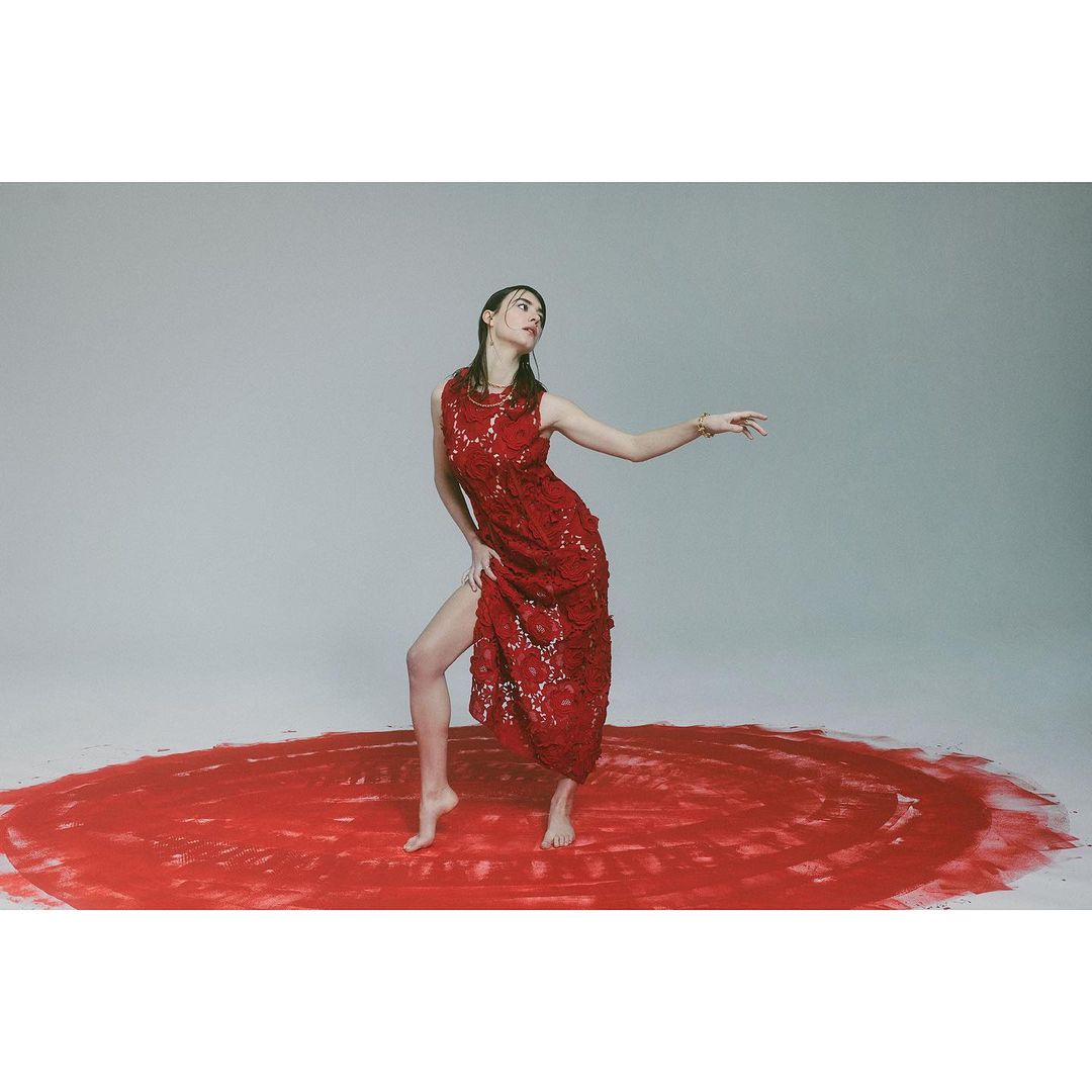 A woman in a red lace dress strikes a pose on a red, textured circle against a seamless grey studio backdrop, creating a striking visual.