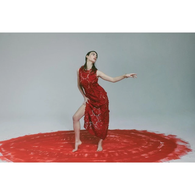 A woman in a red lace dress strikes a pose on a red, textured circle against a seamless grey studio backdrop, creating a striking visual.