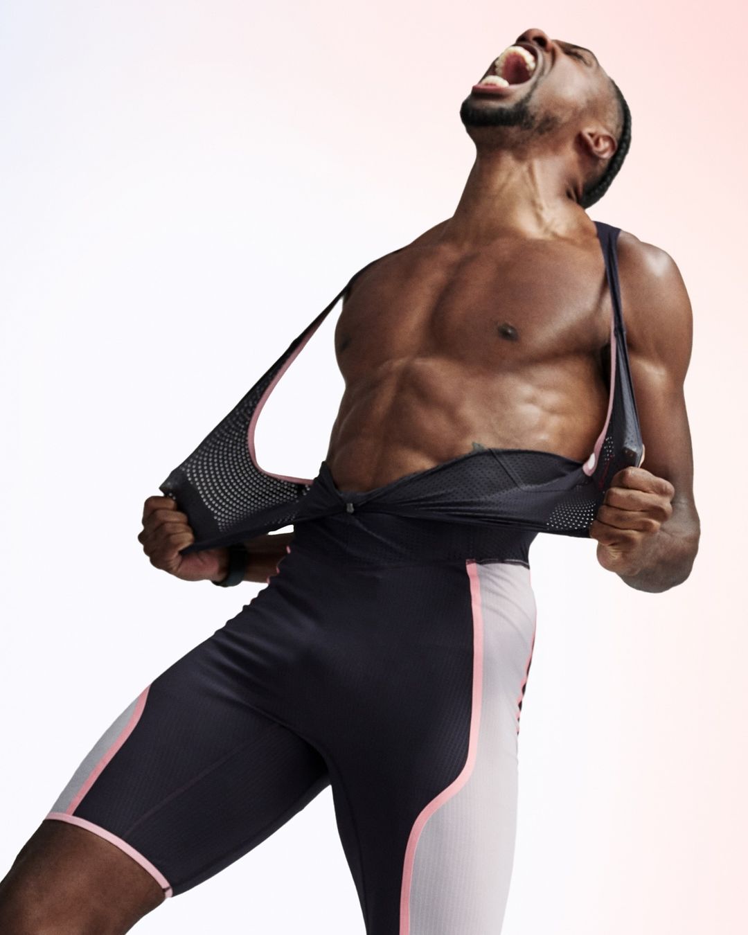 Athletic African-American man in black and pink athletic shorts screams with head tilted back in a fitness pose against white.