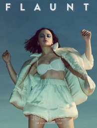 Joey King wearing a white bra and puffy shorts with blue eye shadow against a clear sky