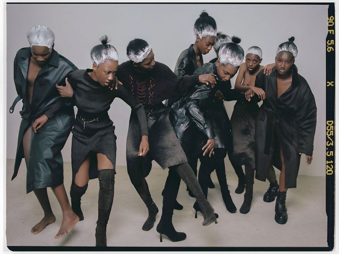 Group of African women with silver-painted hair in various poses wearing black and dark grey outfits in a studio setting.