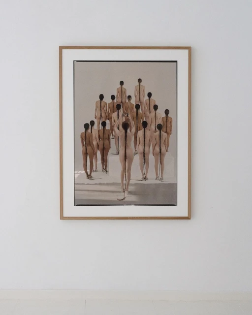 Artistic photograph of a framed print depicting a group of nude figures, seen from behind, with hair braided down their backs.