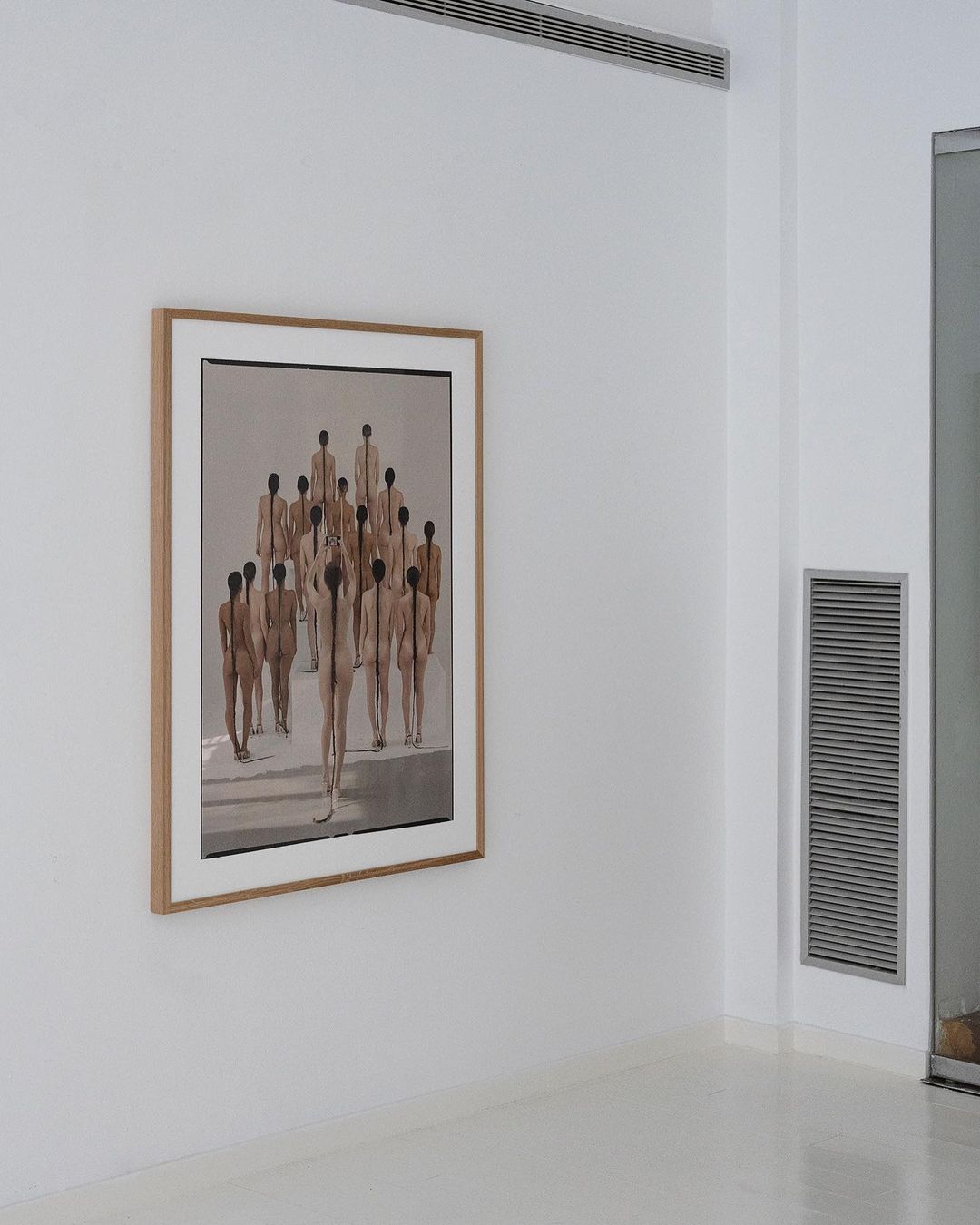 Framed fine art painting of a group of figures hanging on a wall inside of an art gallery with a minimalist design and white walls.