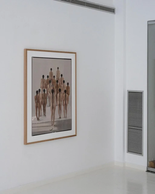 Framed fine art painting of a group of figures hanging on a wall inside of an art gallery with a minimalist design and white walls.