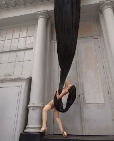Woman with extremely long black hair stretching upward into the sky against a classical building exterior with columns