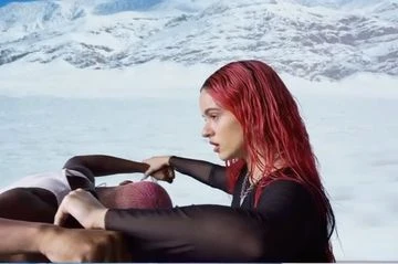 Red-haired woman points at another woman in a black mesh top, against a backdrop of snow-covered mountains, evoking beauty and fashion.
