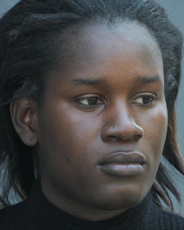 Close-up portrait of a Black woman with dark hair and a neutral expression against a grey background by Carlota Guerrero.
