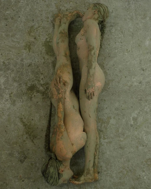 Sculpture of two figures, one standing and the other inverted, both with a rough, earthy texture, against a textured gray background.