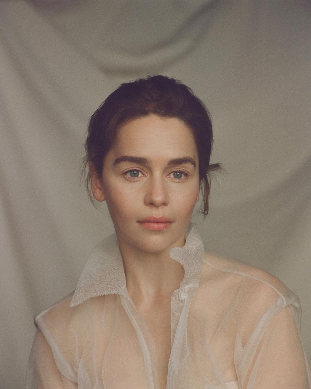 Portrait of adult female with fair skin, neutral facial expression, and sheer white blouse in a photo studio with soft lighting.