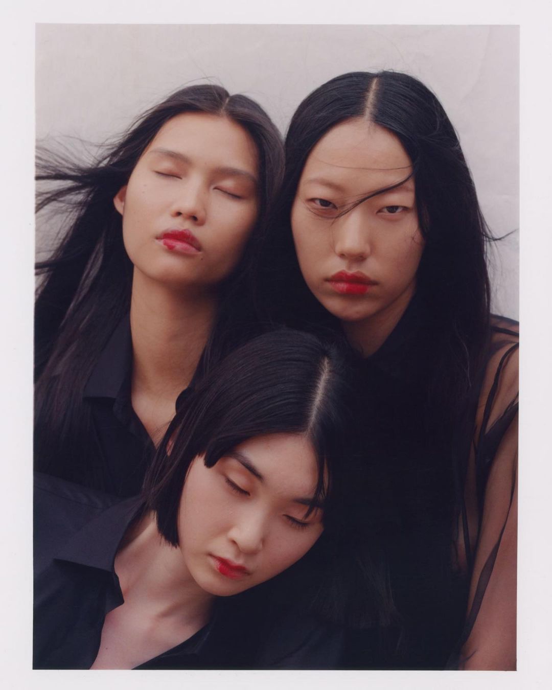 Three Asian women in black tops, red lipstick, and dark hair pose together closely indoors, creating a cohesive and elegant composition.