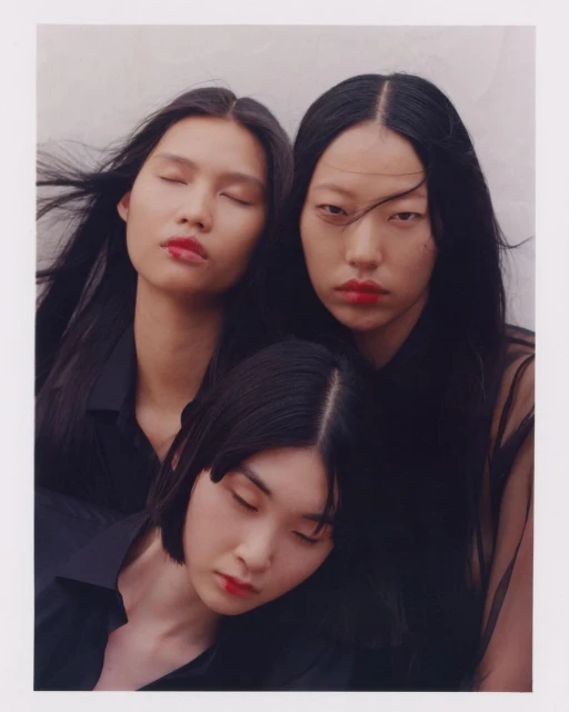 Three Asian women in black tops, red lipstick, and dark hair pose together closely indoors, creating a cohesive and elegant composition.