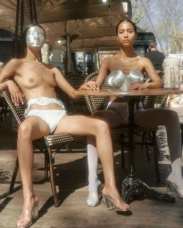 Two women seated at an outdoor café table wearing avant-garde silver accessories by Carlota Guerrero