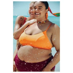 Two women wearing swimsuits smiling outdoors near the ocean with water splashes on the lens, photographed by Carlotta Kohl.