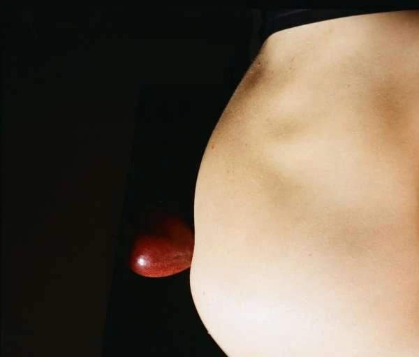 Close-up studio shot of bare human back and a red apple against dark background. Skin texture, light, and form are dominant features.
