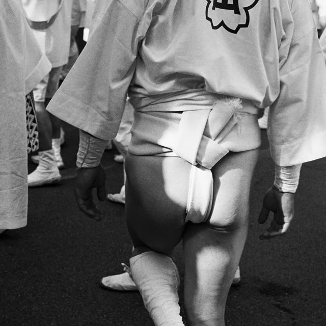 A black and white eye-level shot shows the back view of a person in a traditional white outfit with a large white belt and white socks.