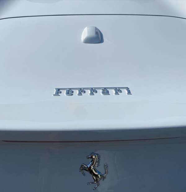 Close-up of a white Ferrari car's rear with the brand name and logo. Automotive photography of a luxury vehicle detail.