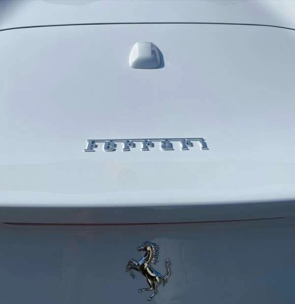 Close-up of a white Ferrari car's rear with the brand name and logo. Automotive photography of a luxury vehicle detail.