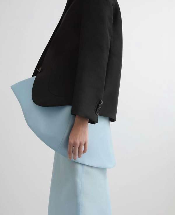 Fashion shot of a woman wearing a black blazer with buttons, and a light blue skirt and peplum top against a white backdrop.