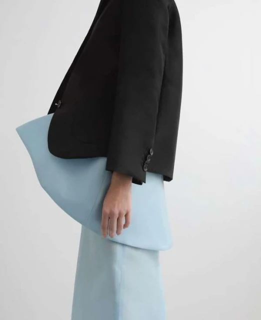 Fashion shot of a woman wearing a black blazer with buttons, and a light blue skirt and peplum top against a white backdrop.