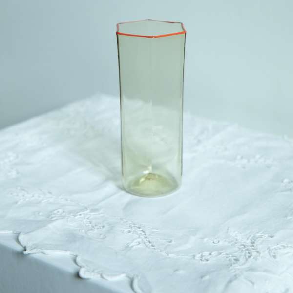 Tall glass vase with hexagonal rim on a white lace tablecloth, soft lighting, and a minimalist studio setting for elegant home decor.