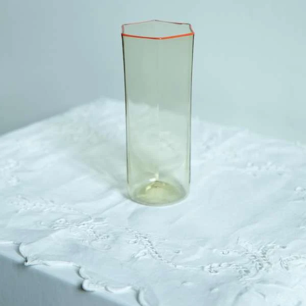 Tall glass vase with hexagonal rim on a white lace tablecloth, soft lighting, and a minimalist studio setting for elegant home decor.