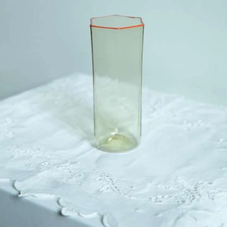 Tall glass vase with hexagonal rim on a white lace tablecloth, soft lighting, and a minimalist studio setting for elegant home decor.