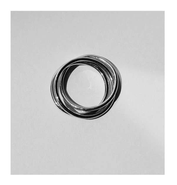 Close-up of a set of interlocking silver rings, lying flat on a white surface with soft lighting and shadows, creating a minimalist aesthetic.