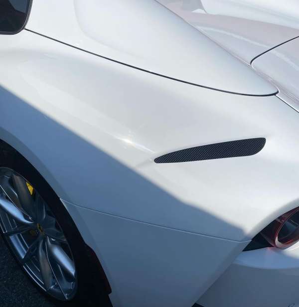Close-up shot of a sleek white sports car showcasing its aerodynamic design, carbon fiber detailing, and shiny silver wheel rims.