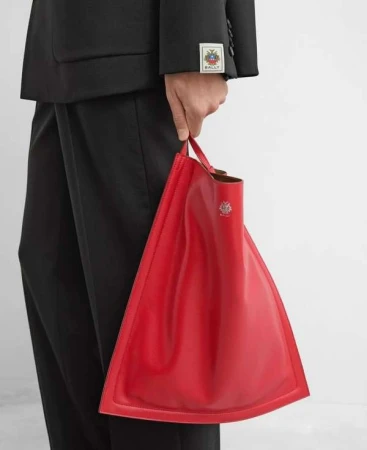 A person holds a red, triangular leather tote bag with the Bally logo, paired with a black suit in a studio setting.