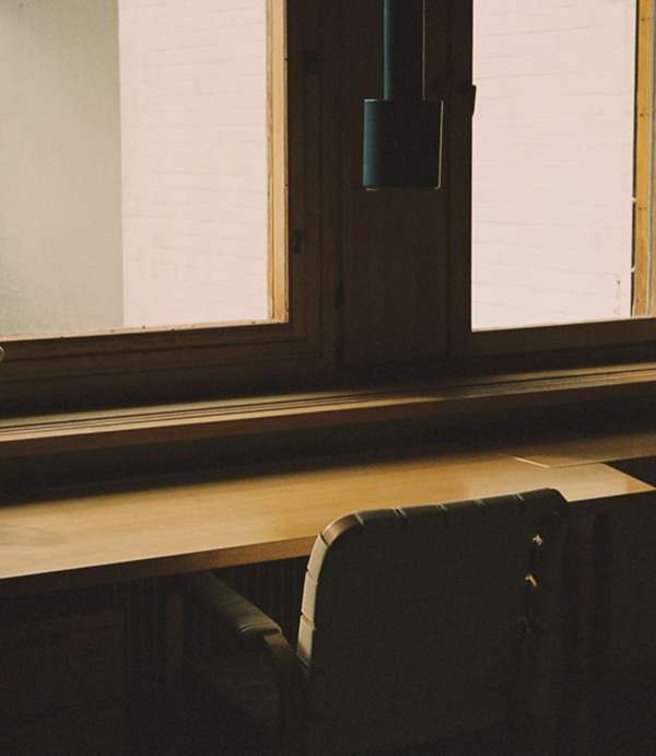 An indoor view showcases a wooden window frame, sill, and a portion of a desk surface with a chair, all bathed in soft, natural light.
